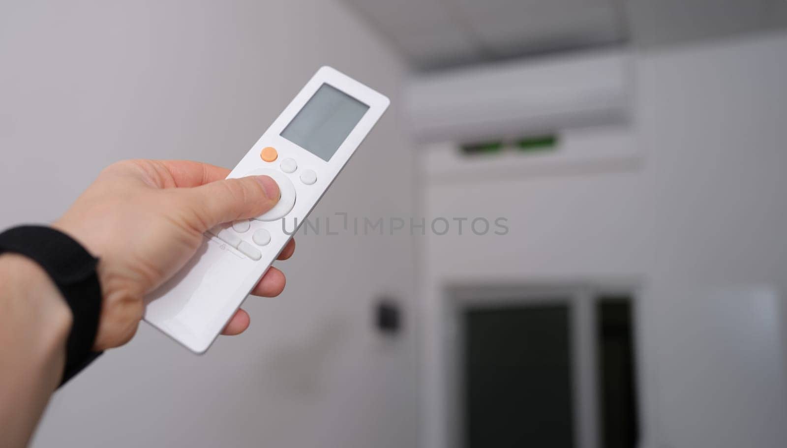 Hand with remote control is directed to air conditioner in room. Climate control indoor concept