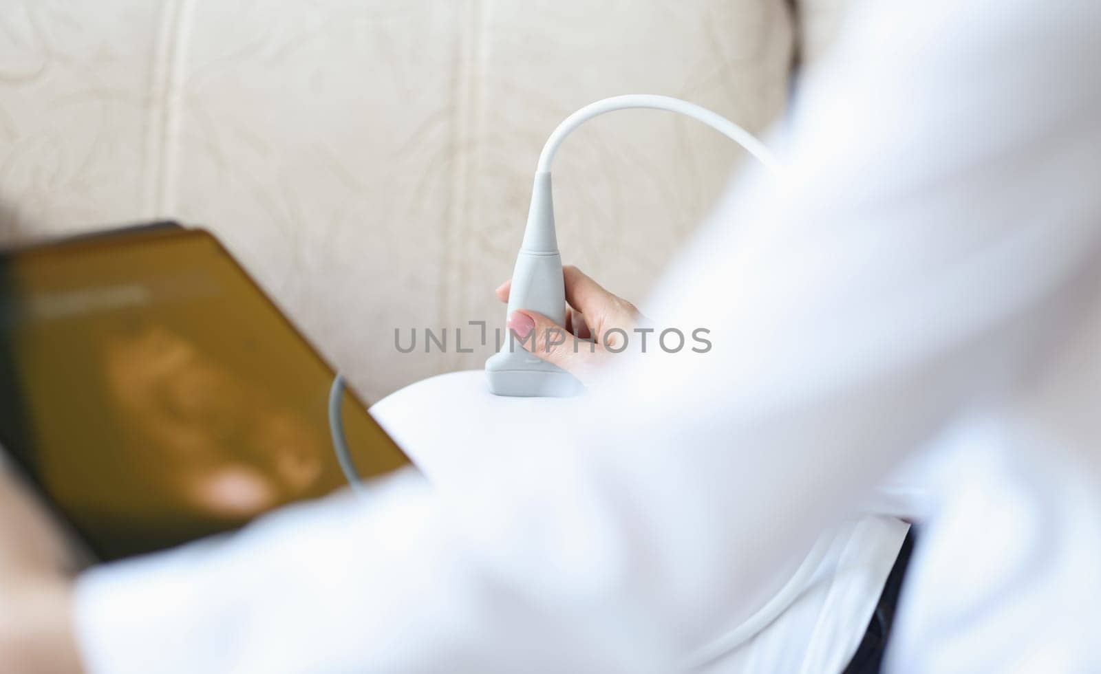 Doctor with ultrasound equipment during ultrasound medical examination of abdomen. Examination of fetus during pregnancy at home