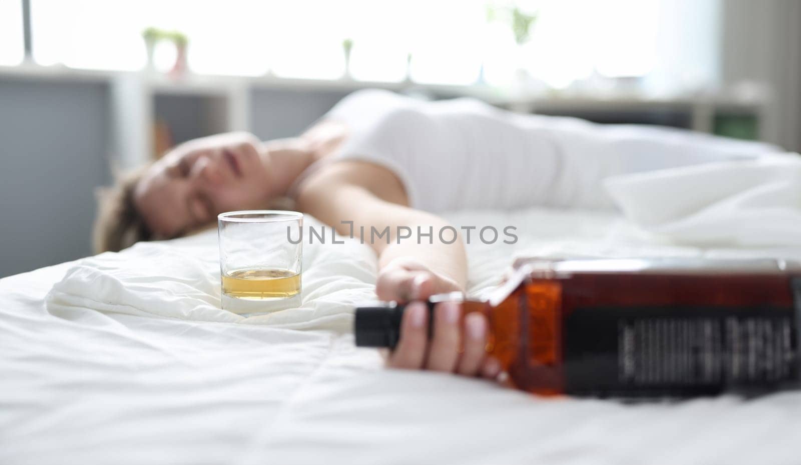 Drunk young woman lies in bed in bottle of alcohol by kuprevich