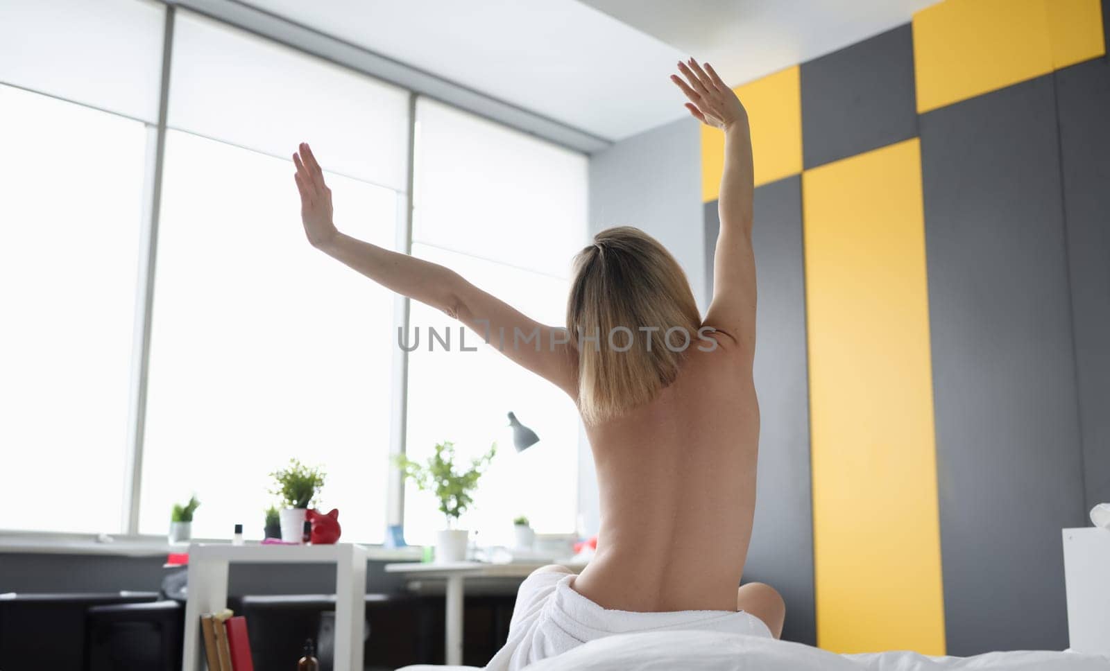 Rear view of naked woman stretching out arms after waking up in morning at home by kuprevich