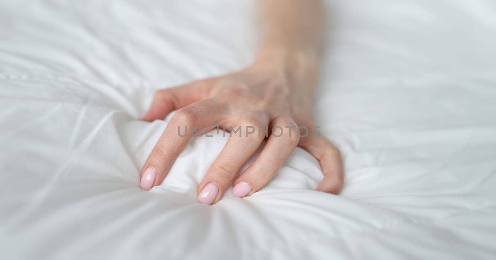 Woman hand tightly grips white sheet on bed by kuprevich