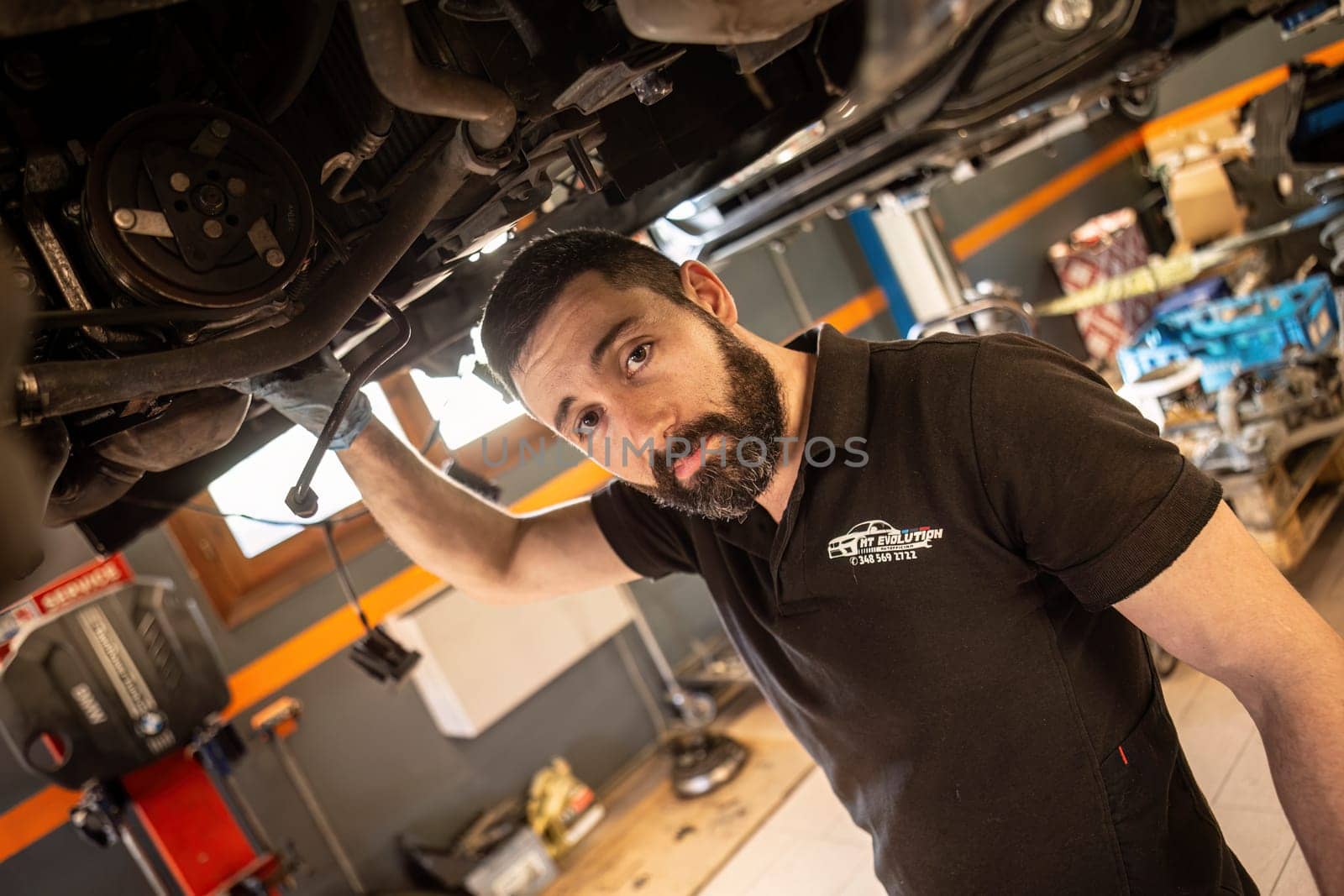 Milan, Italy 9 April 2024: Skilled mechanic repairing vehicle underneath, maintenance work in garage.