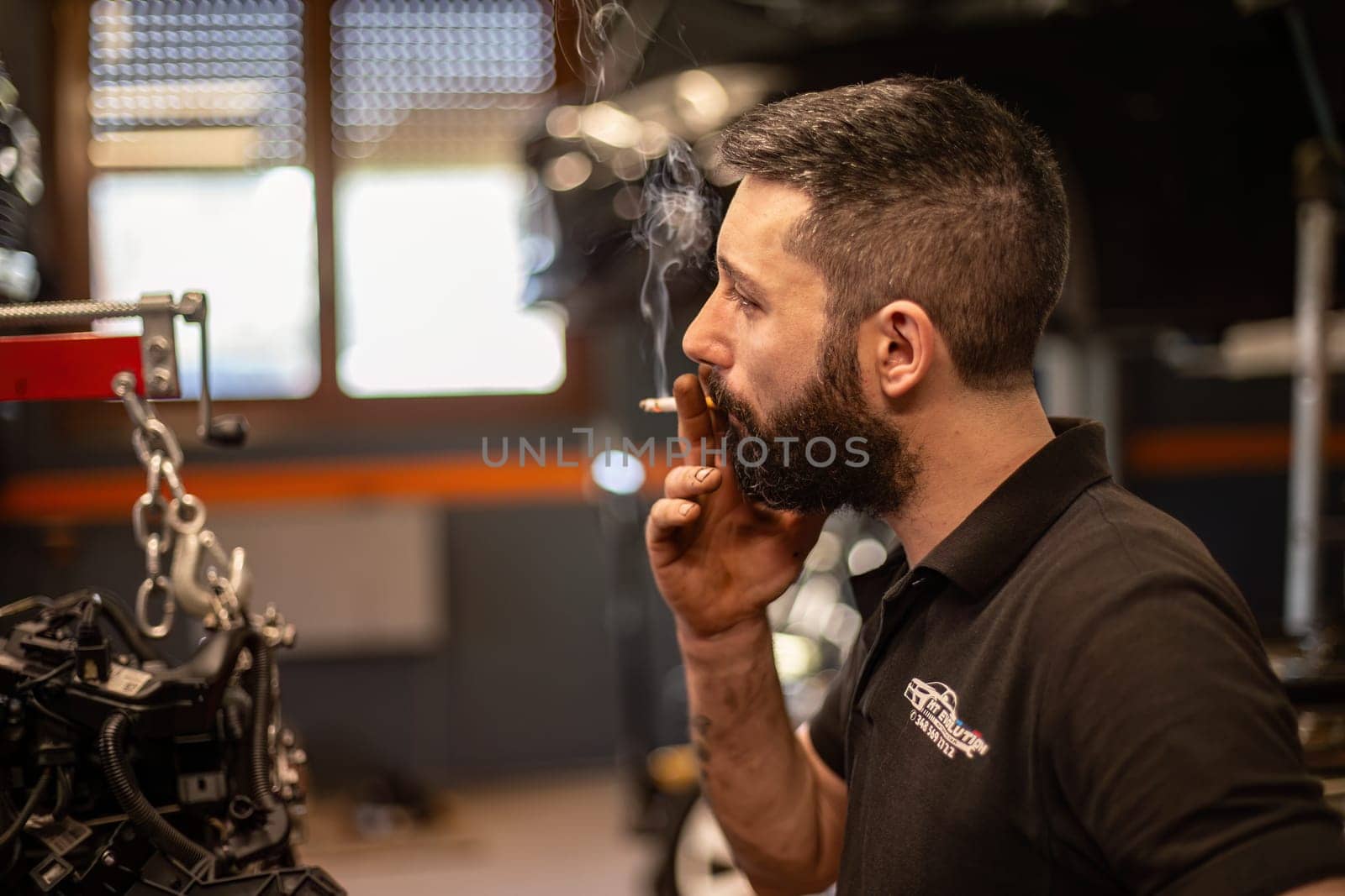 Milan, Italy 9 April 2024: Mechanic takes a cigarette break amid hard work in workshop setting.