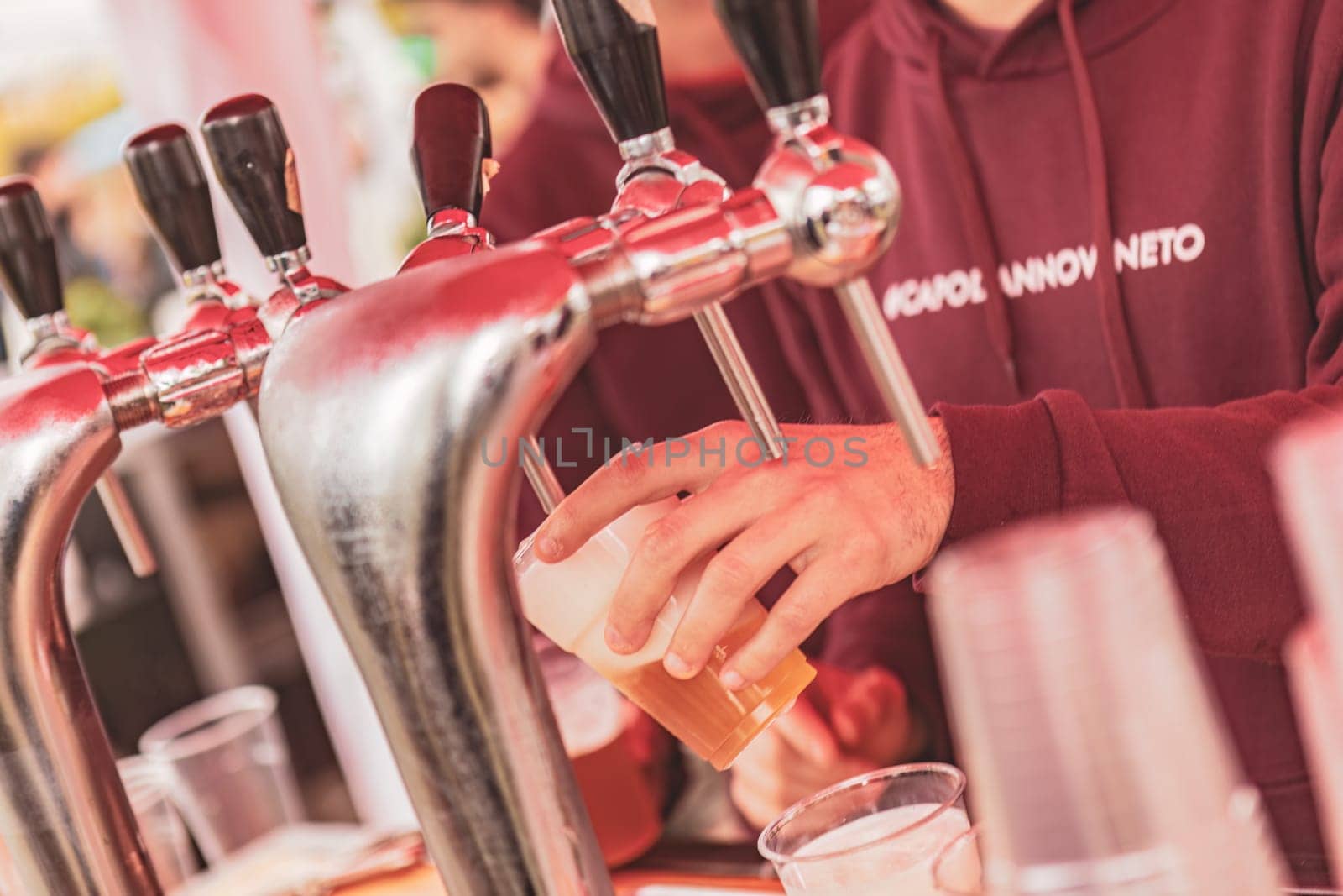 Milan, Italy 1 April 2024: A man with a beard and a plaid shirt is filling a glass of beer from a tap at a dimly lit bar.