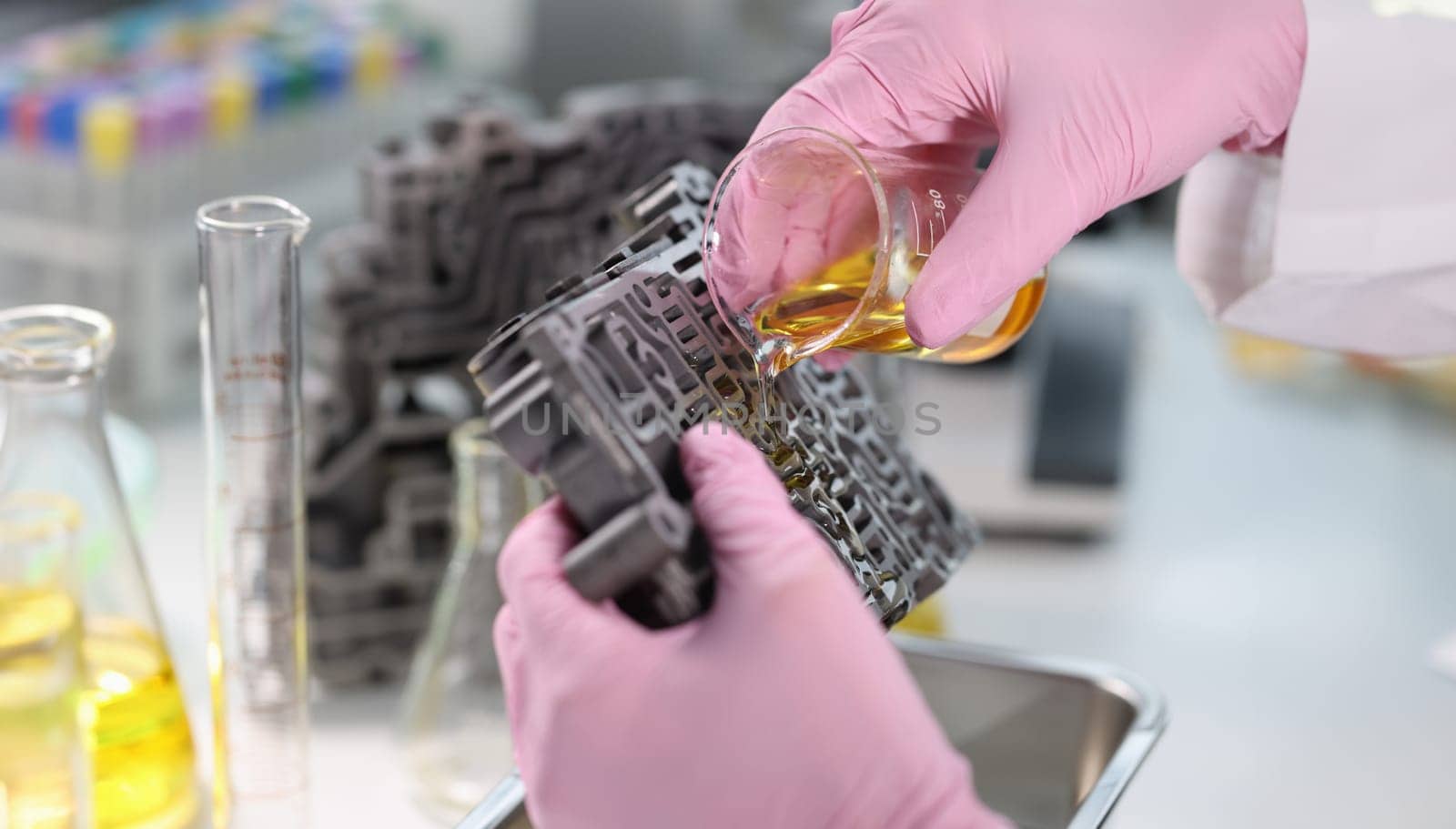 Scientist from chemical flask pours oil on gearbox valve body. Lubricants for automotive parts