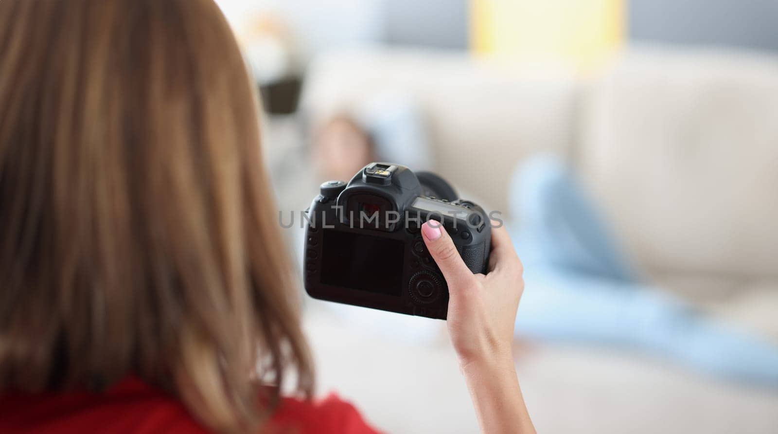 Woman holds professional black camera in hands and photographs model at home by kuprevich