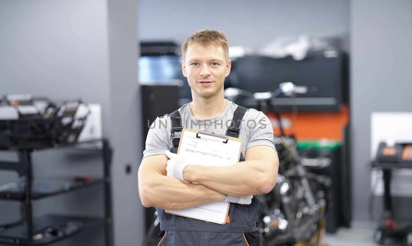 Male car mechanic holding clipboard in auto workshop. Car repair and maintenance services concept