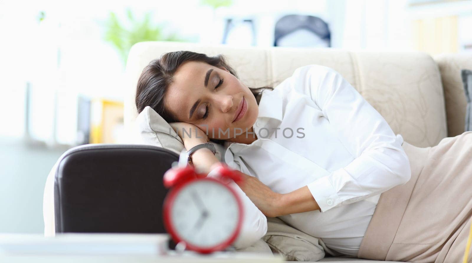 Young woman sleeps on sofa next to alarm clock by kuprevich