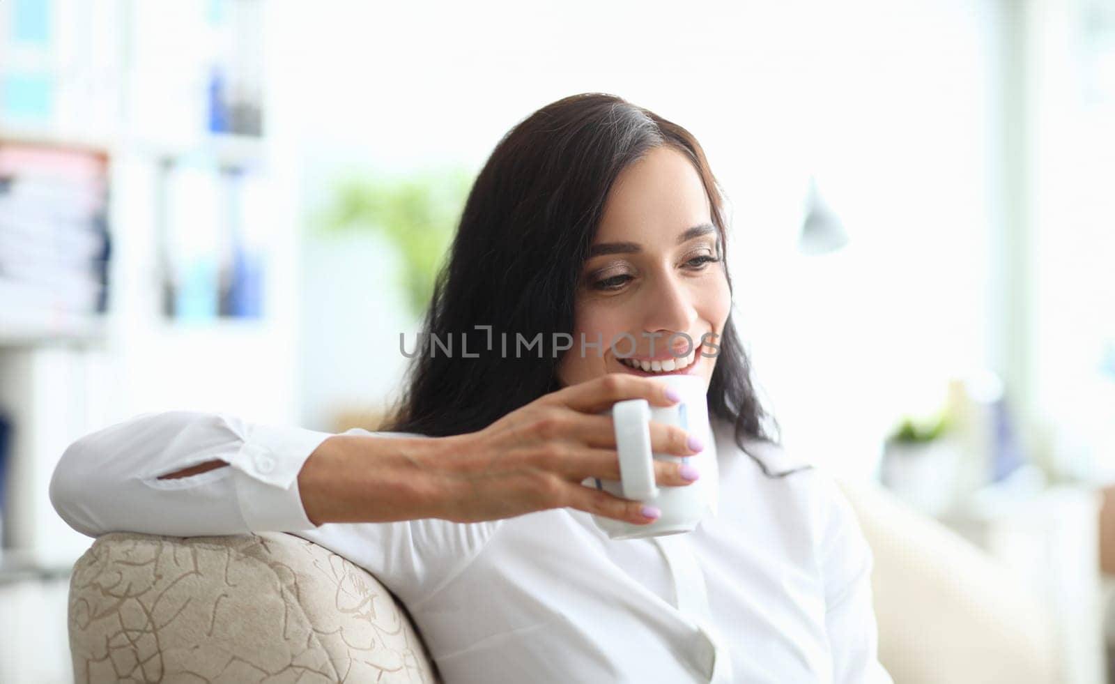 Young woman drinks from cup while sitting on couch. Drinking regimen of day concept