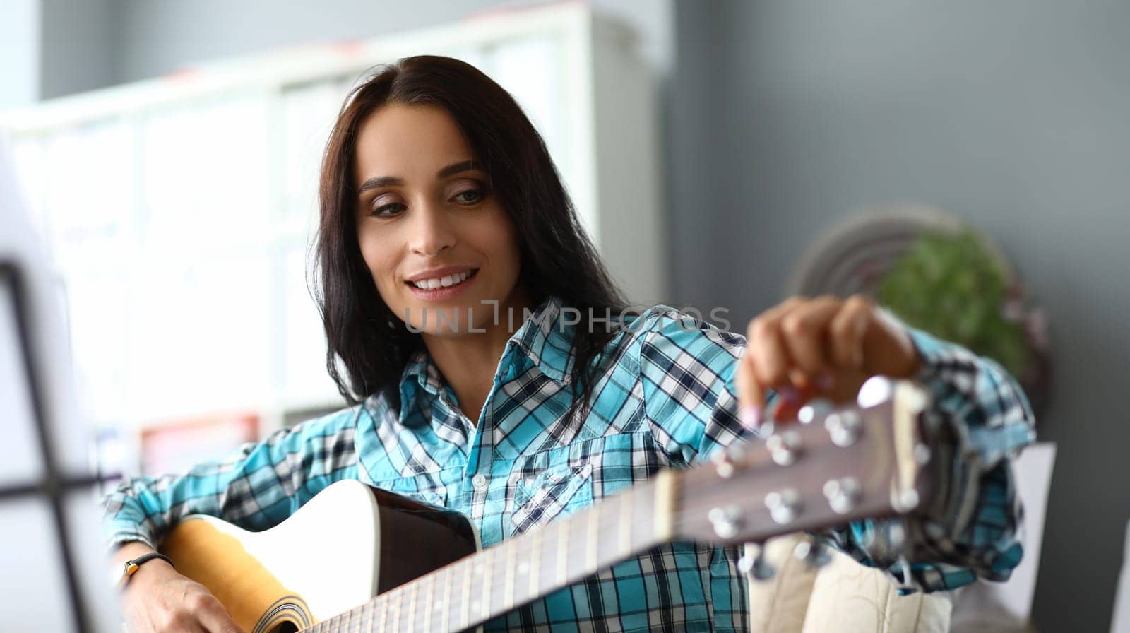 Young woman tunes guitar for music practice. Learning to play guitar concept