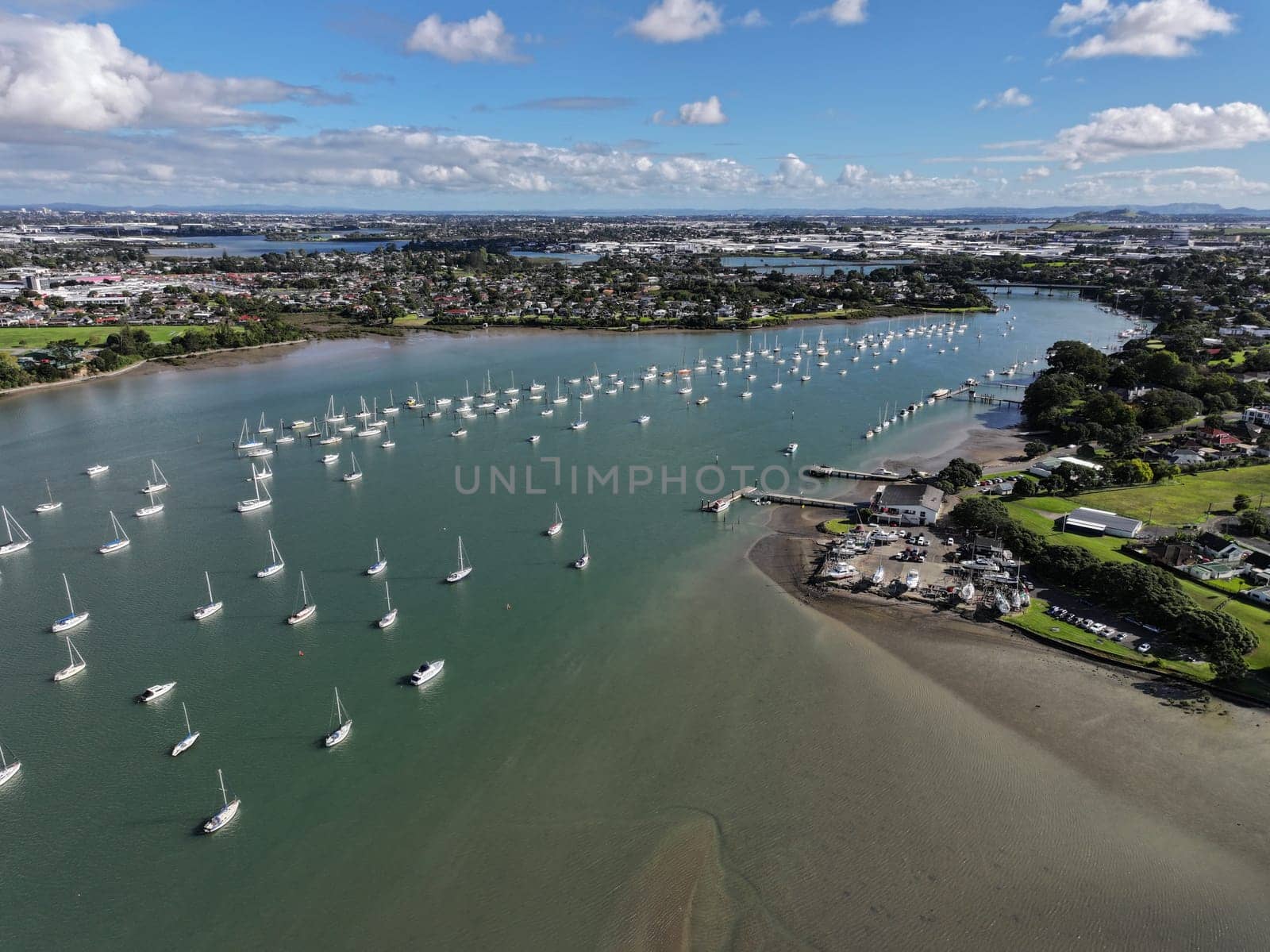 4k drone footage of the Tamaki river at midday, panning across the city scenery. Sailboats on moorings line up the river and marina in New Zealand