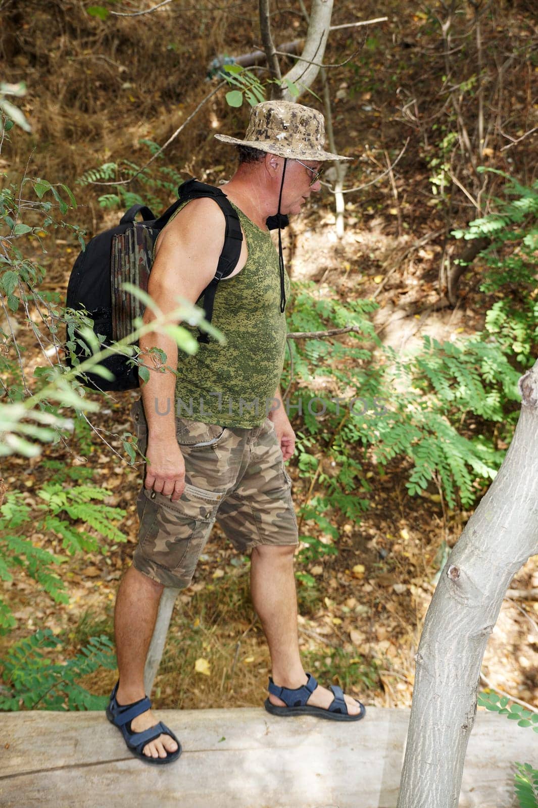 A man with a backpack hiking along a forest path in camouflage shorts.