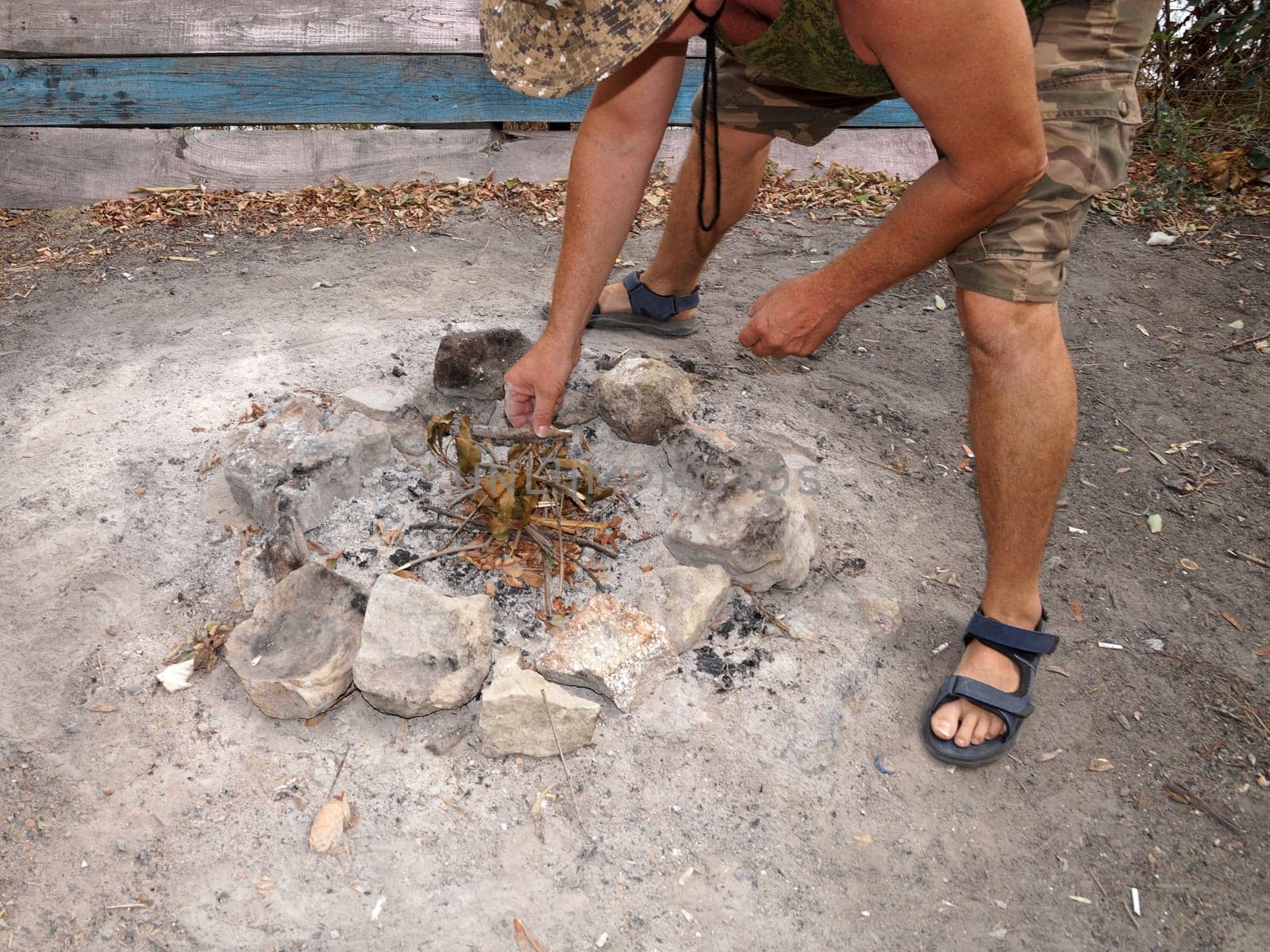 man preparing campfire with stones and twigs outdoors.