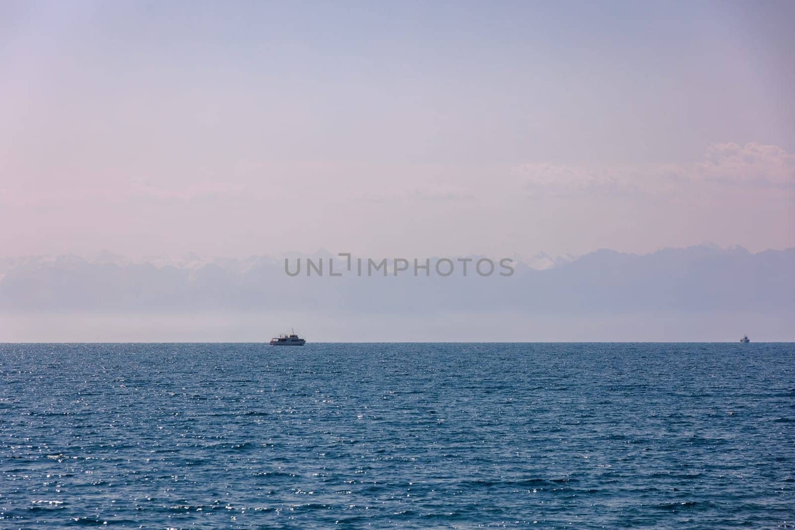 Two boats with Kyrgyzstan flag on Issyk-Kul lake at summer day with mountains on horizon.