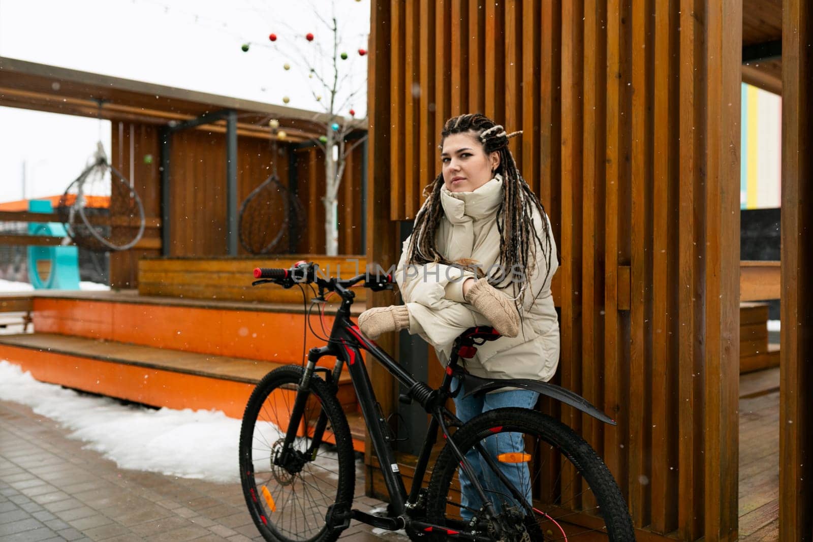 A woman with dreadlocks is seated on a bicycle, appearing relaxed and confident. She is wearing casual clothing, and the bike is stationary in an urban setting. The focus is on her unique hair and the mode of transportation she is using.