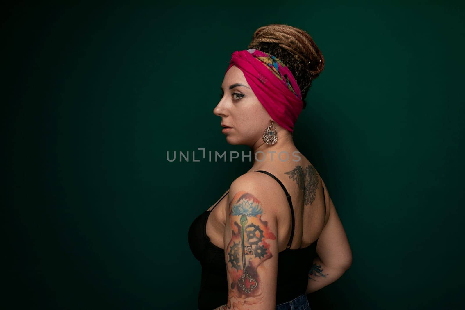 A woman with tattoos on her arms wearing a pink headband. She is standing confidently and looking directly at the camera.