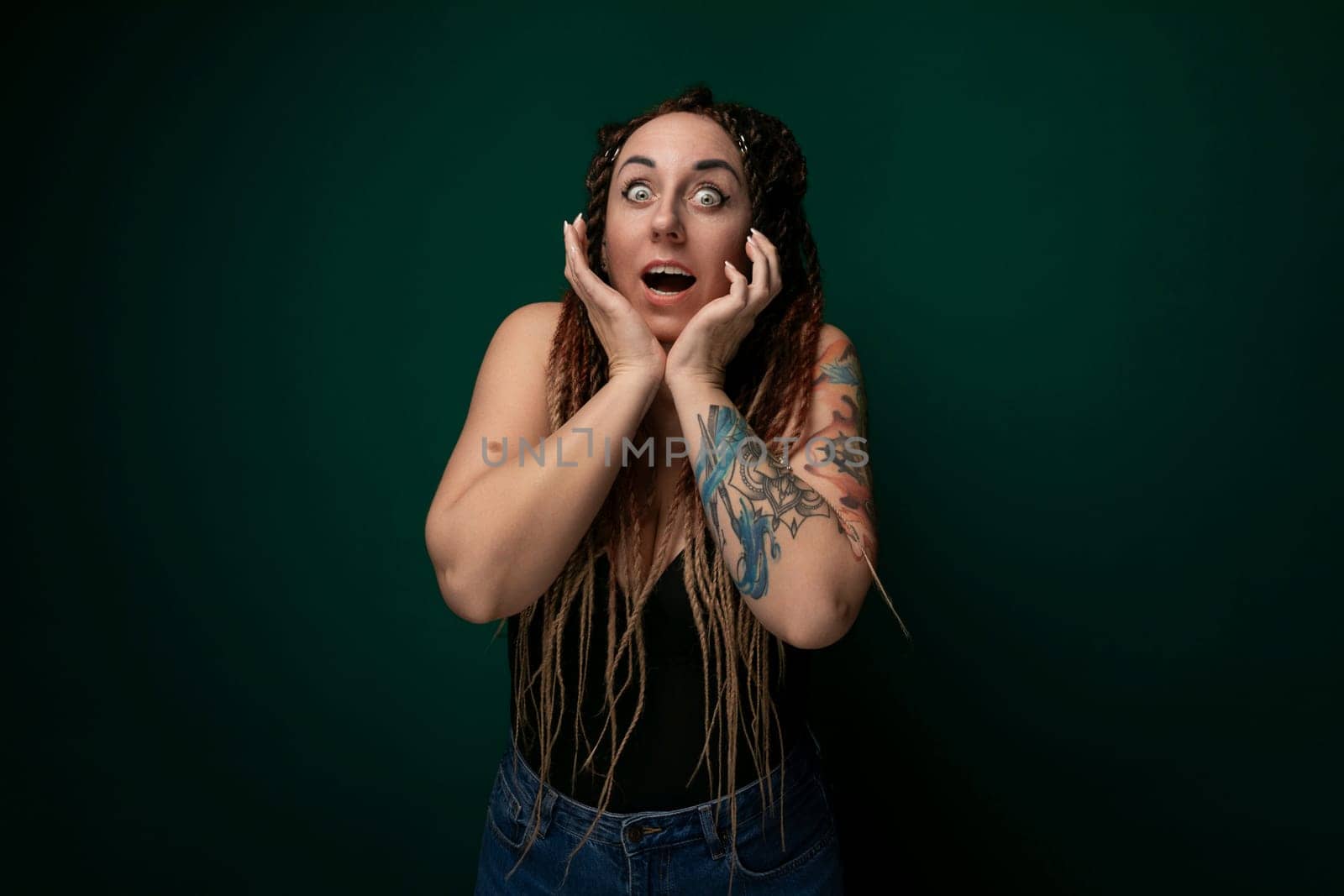 A woman with dreadlocks is shown covering her face with her hands. Her facial features are obscured, emphasizing a sense of privacy or introspection. The dreadlocks cascade down her shoulders, adding texture to the image.