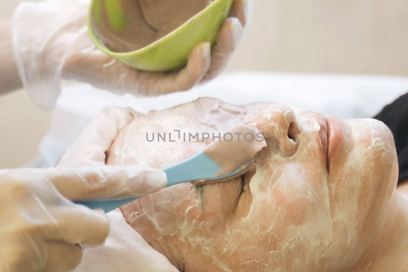 A woman is having a facial mask applied to her face in a spa setting. The skincare professional is gently smoothing on the mask for a revitalizing treatment.