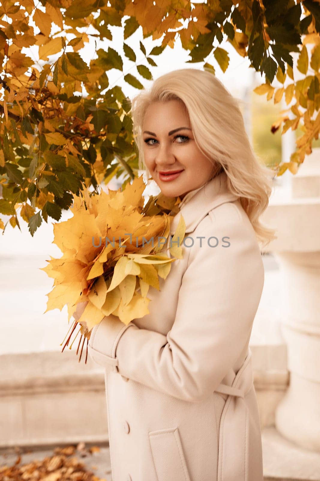 A blonde woman is holding a bouquet of yellow leaves. She is smiling and she is happy