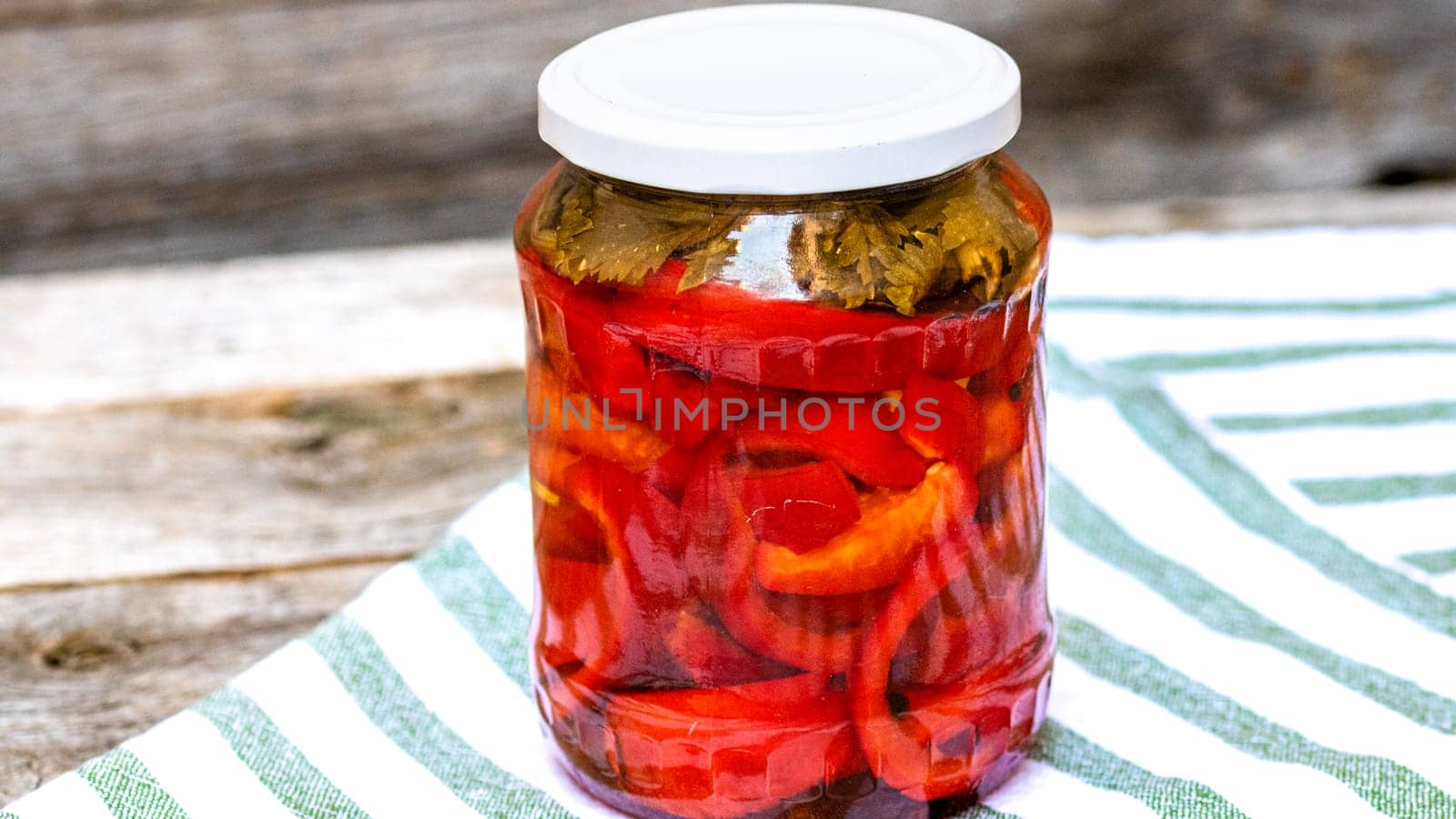 Glass jar with pickled red bell peppers.Preserved food concept, canned vegetables isolated in a rustic composition. by vladispas