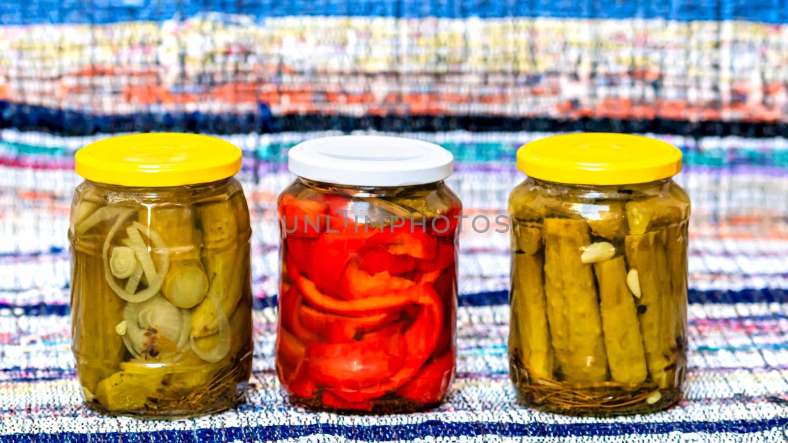  Glass jars with pickled red bell peppers and pickled cucumbers (pickles) isolated. Jars with variety of pickled vegetables. Preserved food concept in a rustic composition. by vladispas