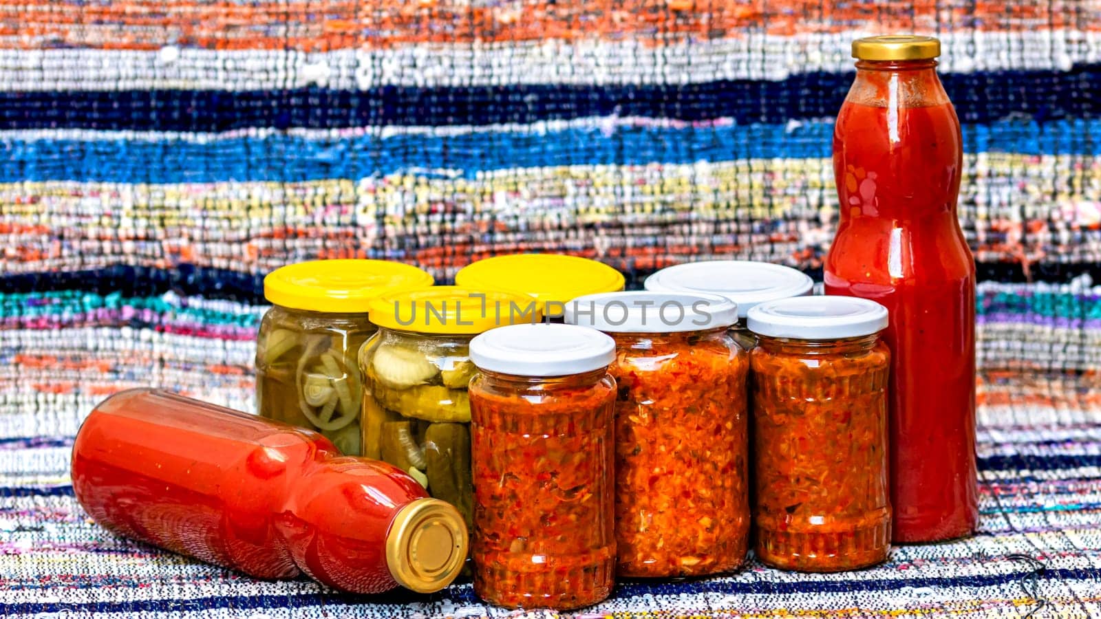 Glass jars with pickled red bell peppers and pickled cucumbers (pickles) isolated. Jars with variety of pickled vegetables, jars with zacusca and bottles with tomatoes sauce. Preserved food concept. by vladispas