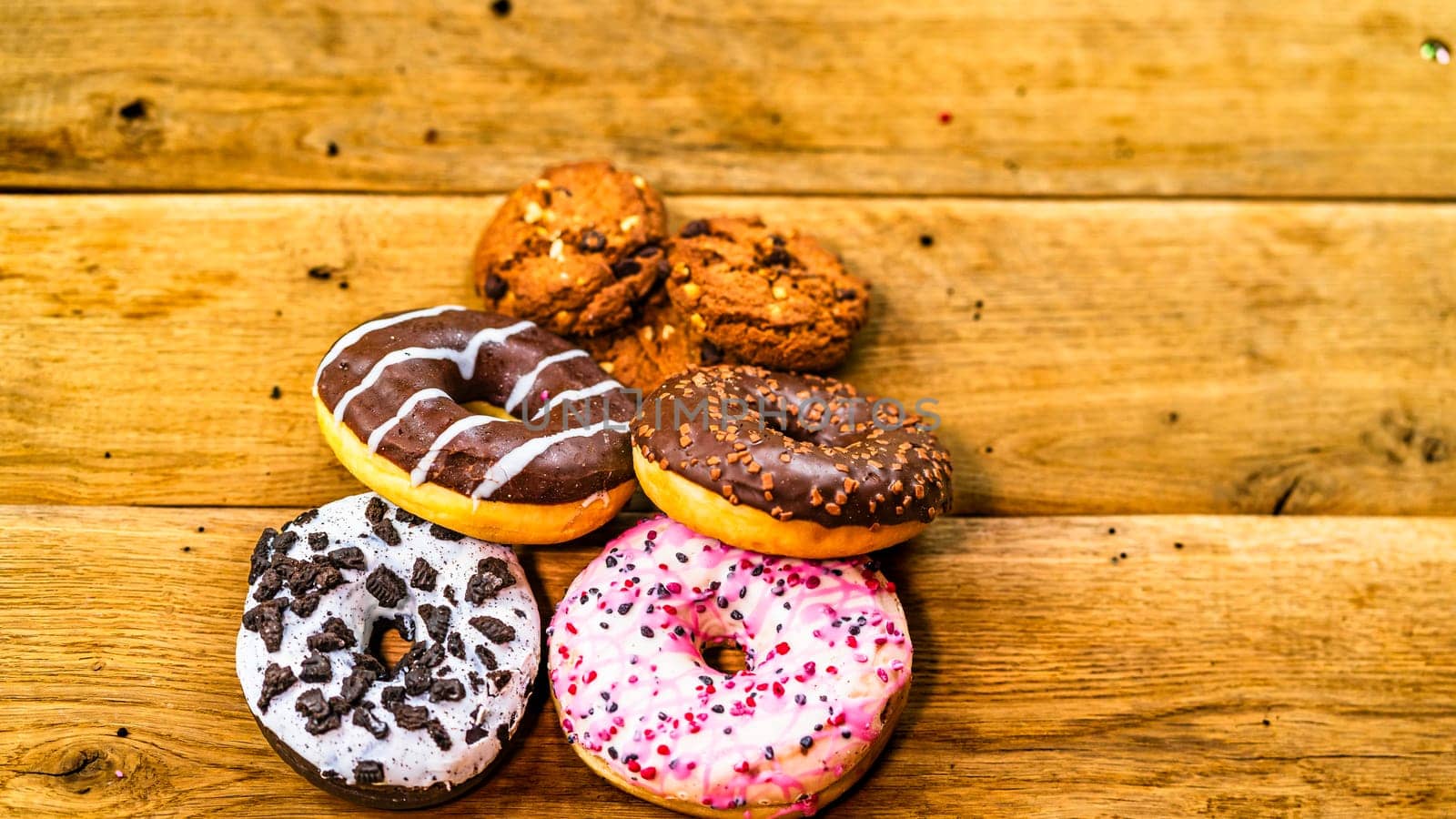 Colorful donuts and biscuits on wooden table. Sweet icing sugar food with glazed sprinkles, doughnut with chocolate frosting. Top view with copy space by vladispas