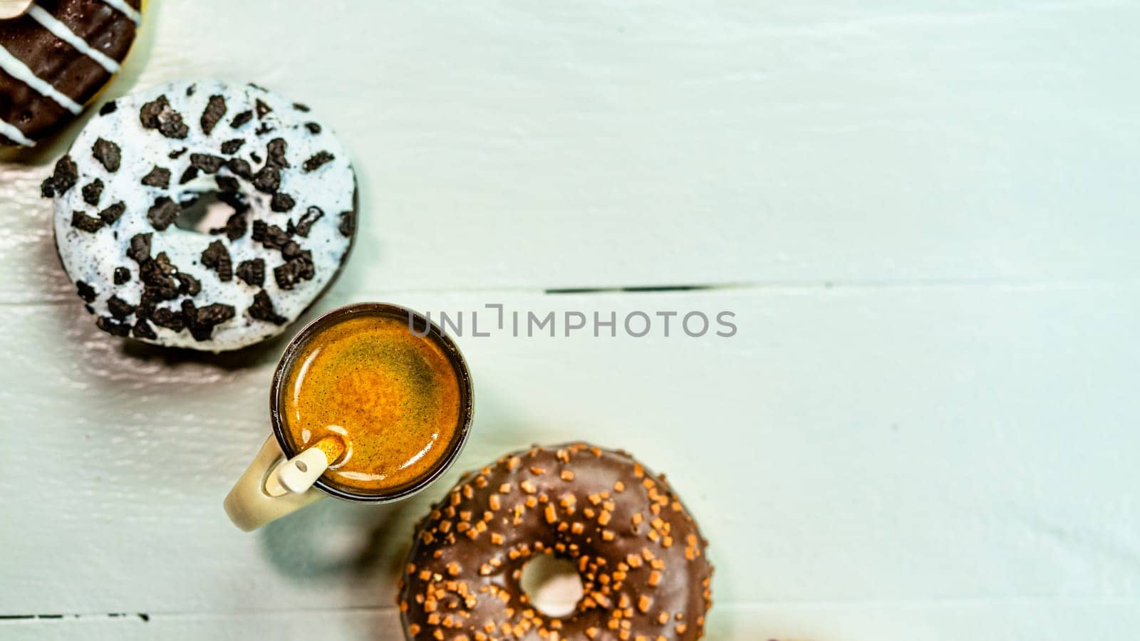 Colorful donuts and coffee cup on white wooden table. Sweet bakery with glazed sprinkles, breakfast concept. Top view with copy space by vladispas