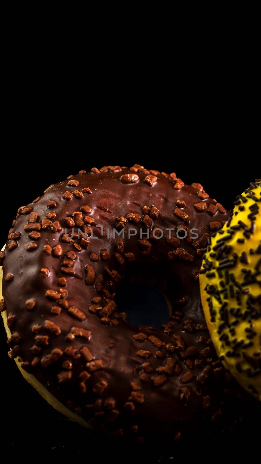 Fresh tasty colored donuts with sprinkles on black background by vladispas