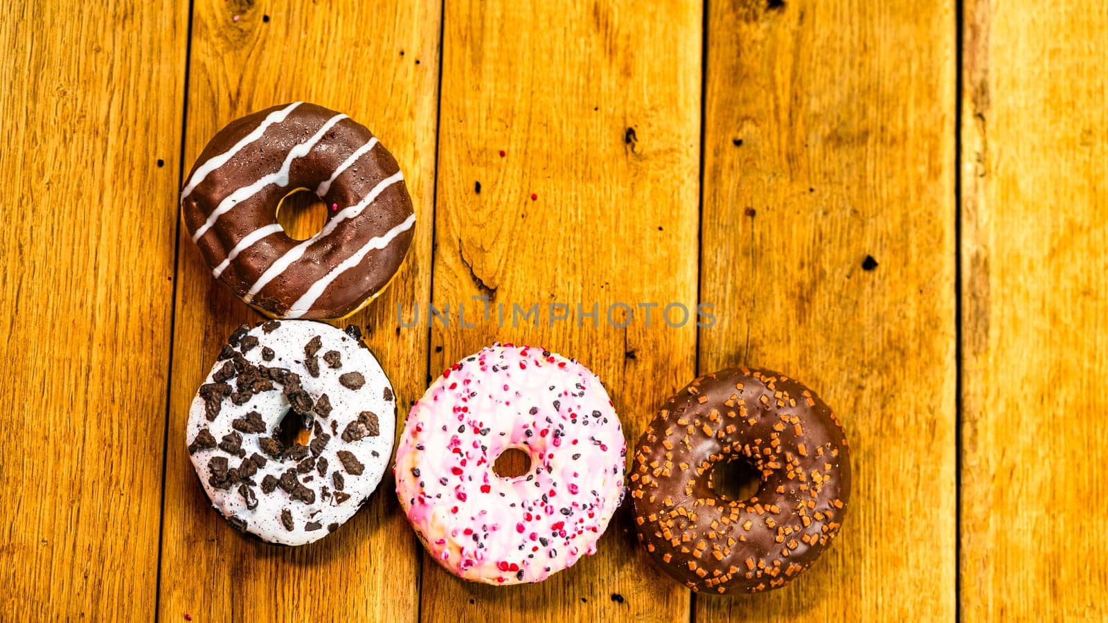 Colorful donuts on wooden table. Sweet icing sugar food with glazed sprinkles, doughnut with chocolate frosting. Top view with copy space