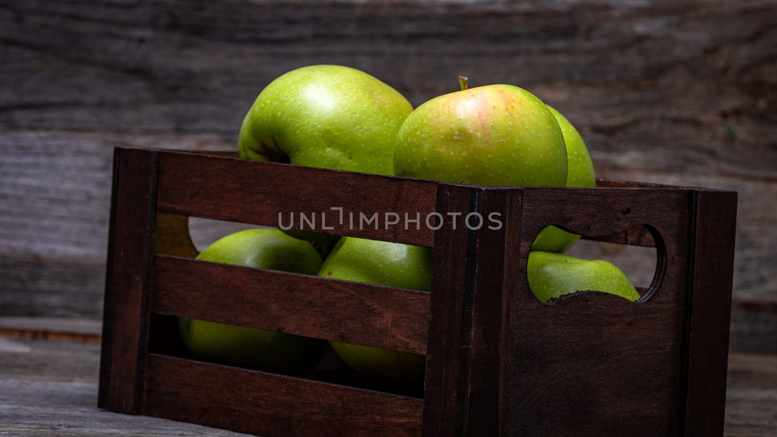 Wooden crate with ripe green apples on wooden table. by vladispas