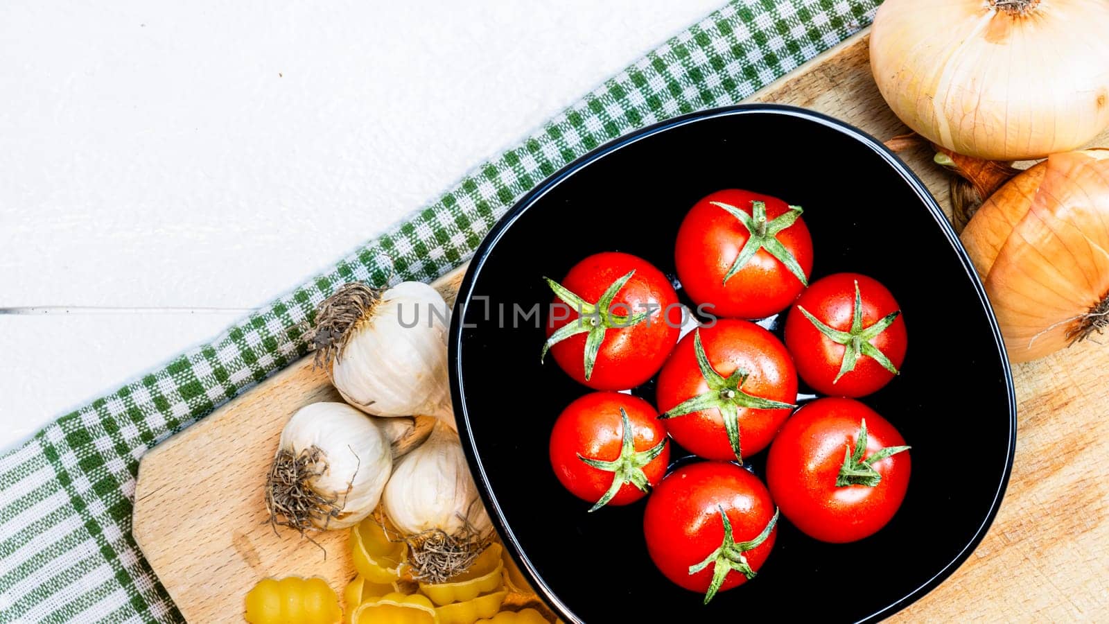 Top view of onions, garlic and fresh ripe cherry tomatoes on a rustic white wooden table. Ingredients and food concept