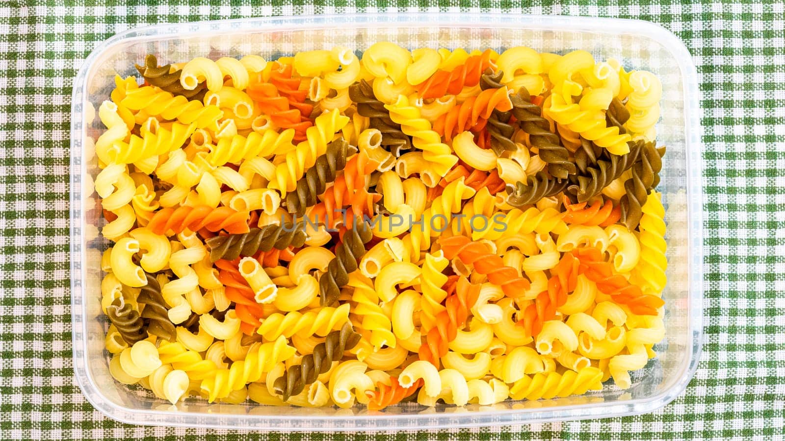 Tricolore fusilli, raw Italian pasta in plastic container, close up isolated in rustic composition