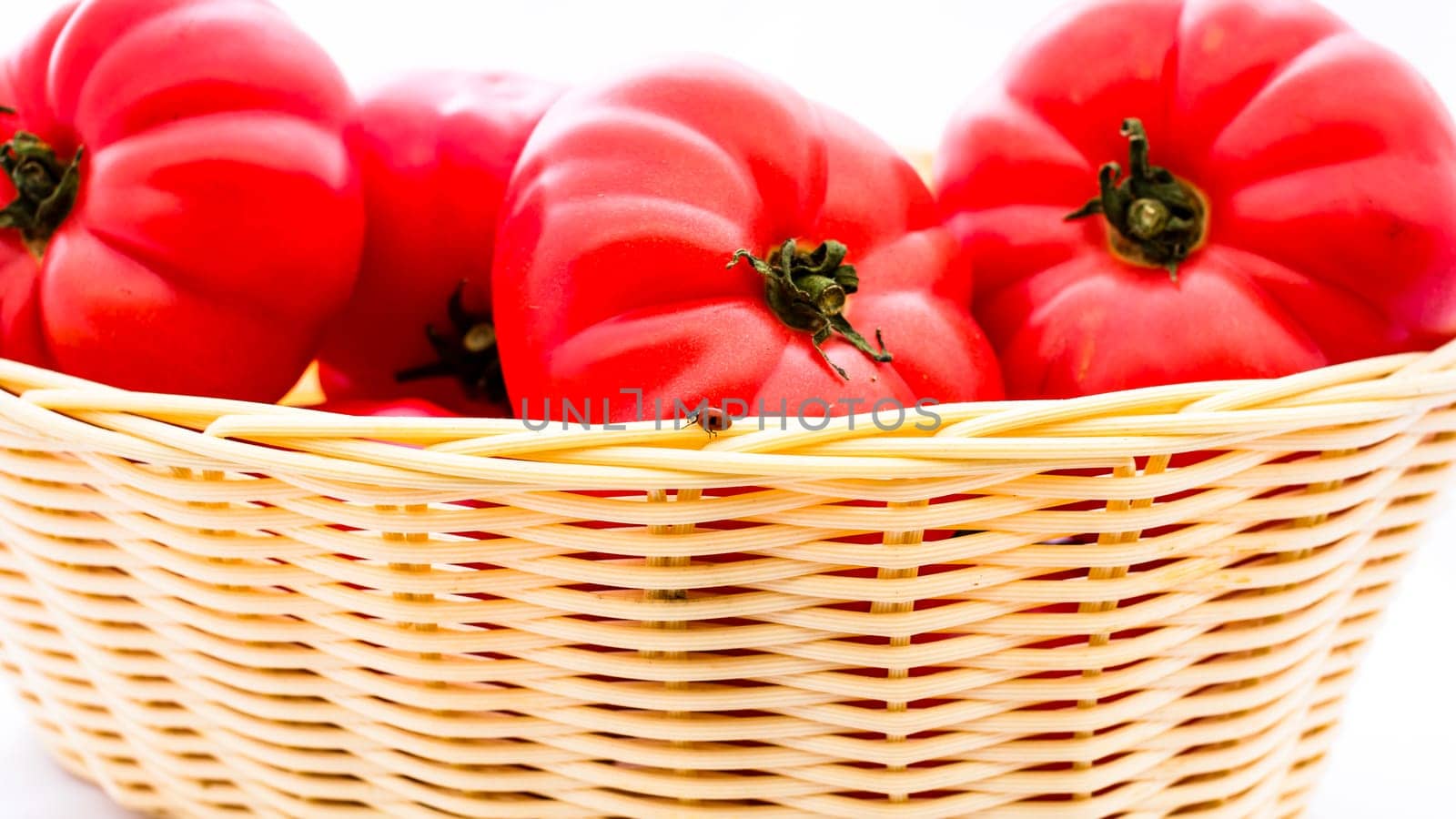 Fresh and tasty red tomatoes in wicker basket isolated by vladispas