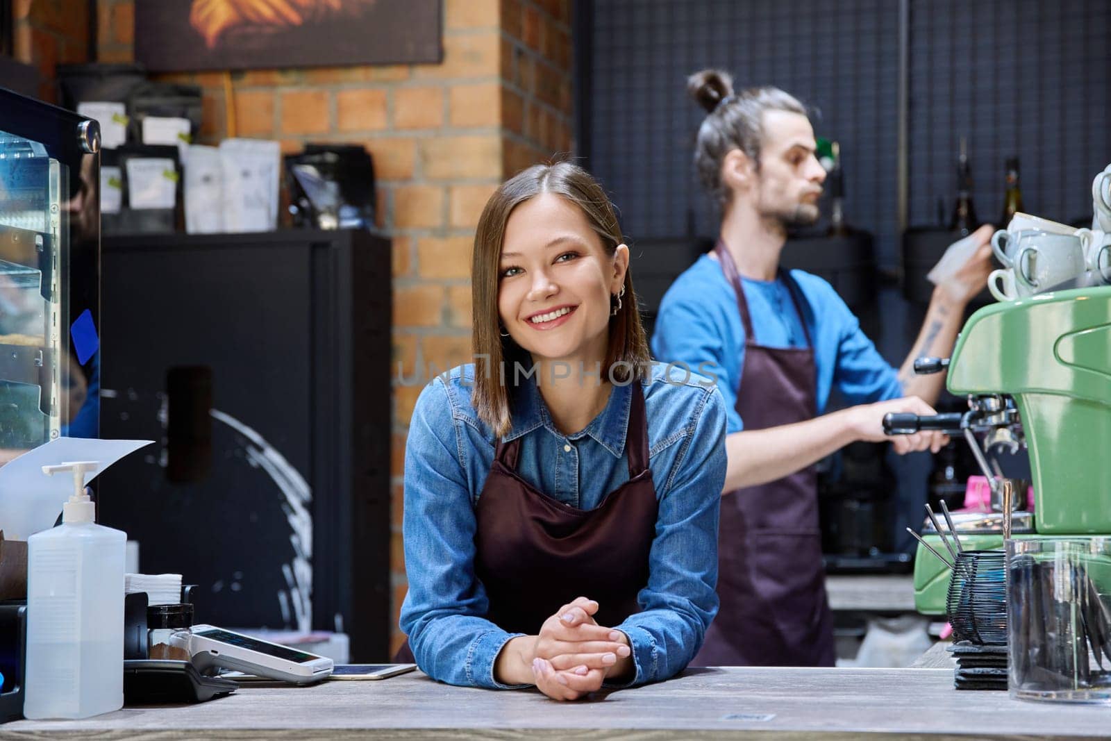 Business team colleagues partners young man woman in aprons working together in workplace behind counter in restaurant coffee shop cafeteria. Cooperation staff partnership teamwork work small business