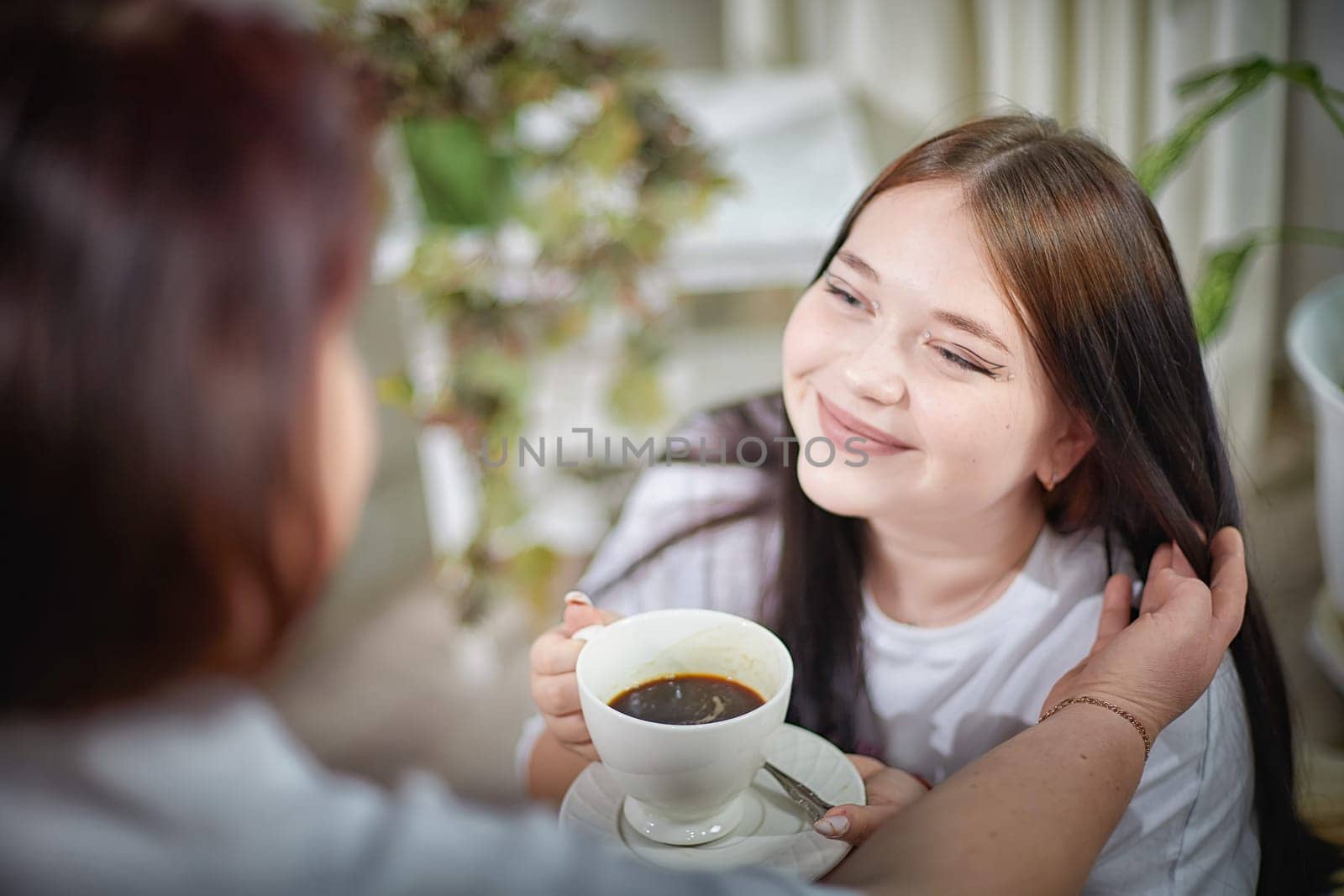 Happy Overweight family with mother and daughter drinking tea or coffee in room. Middle aged woman and teenager girl having fun and joy