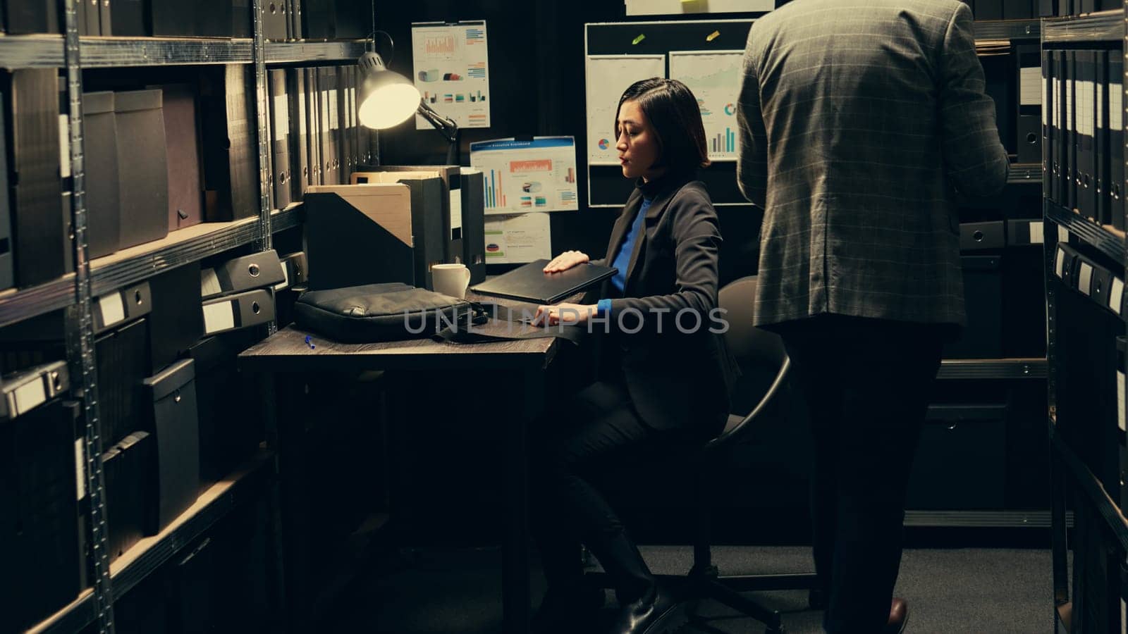 Woman detective arriving at job to solve police investigation, entering archive room to work on criminal case. Asian investigator recreating crime scenes based on archived evidence. Camera B.