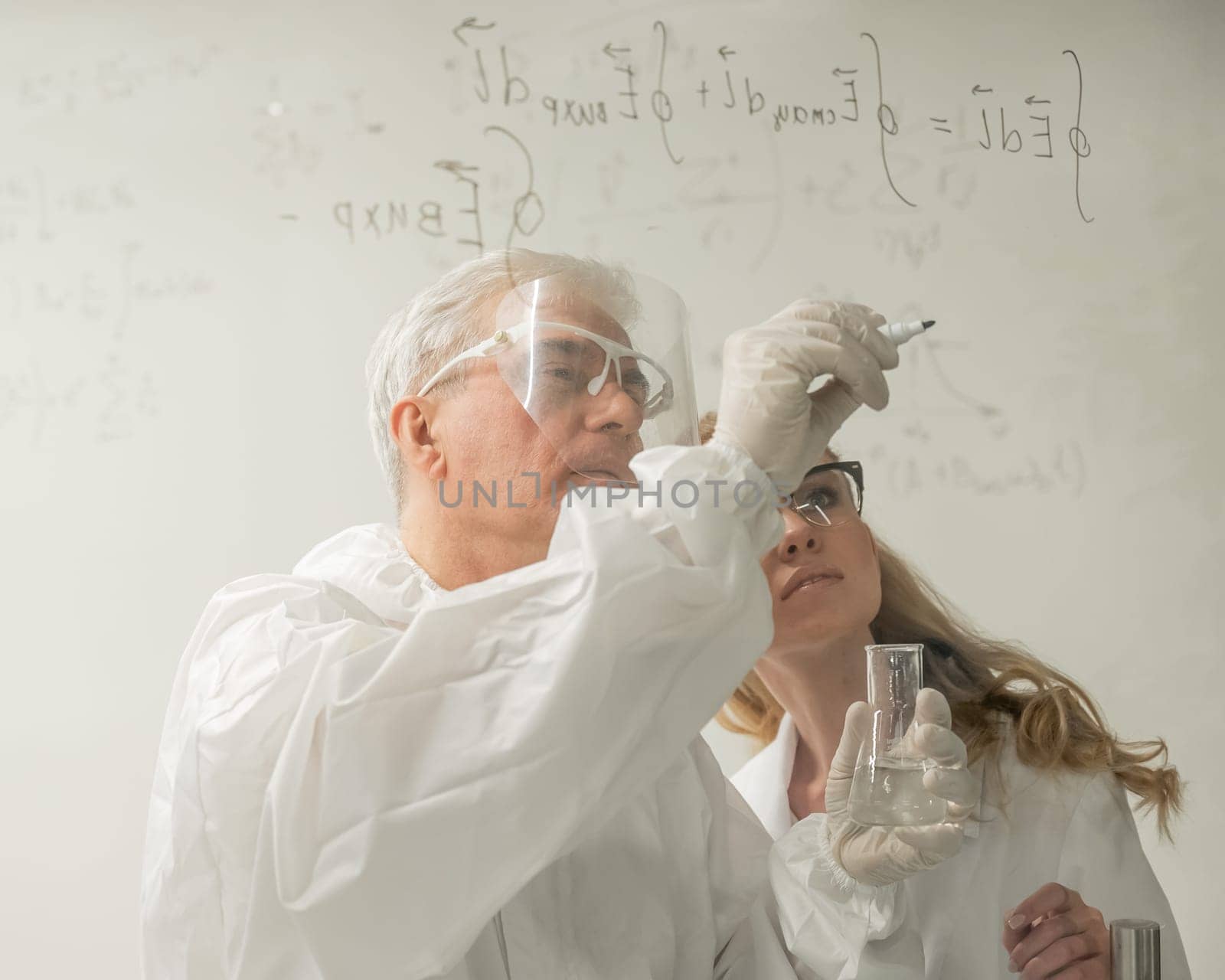 Two chemist colleagues write formulas on glass. Caucasian elderly man and young woman brainstorming. by mrwed54