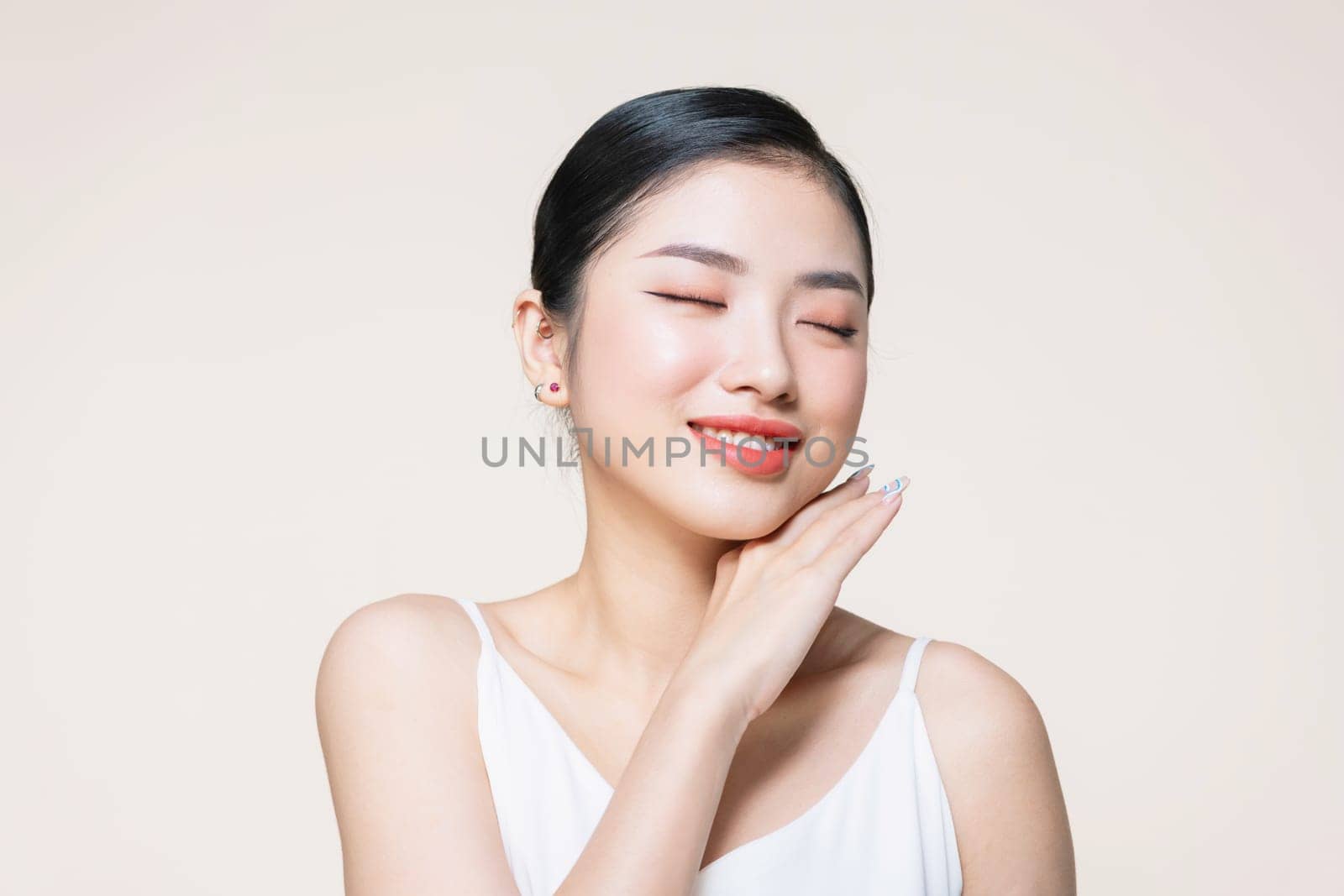 The beautiful Asian woman showing clear skin on the beige background.