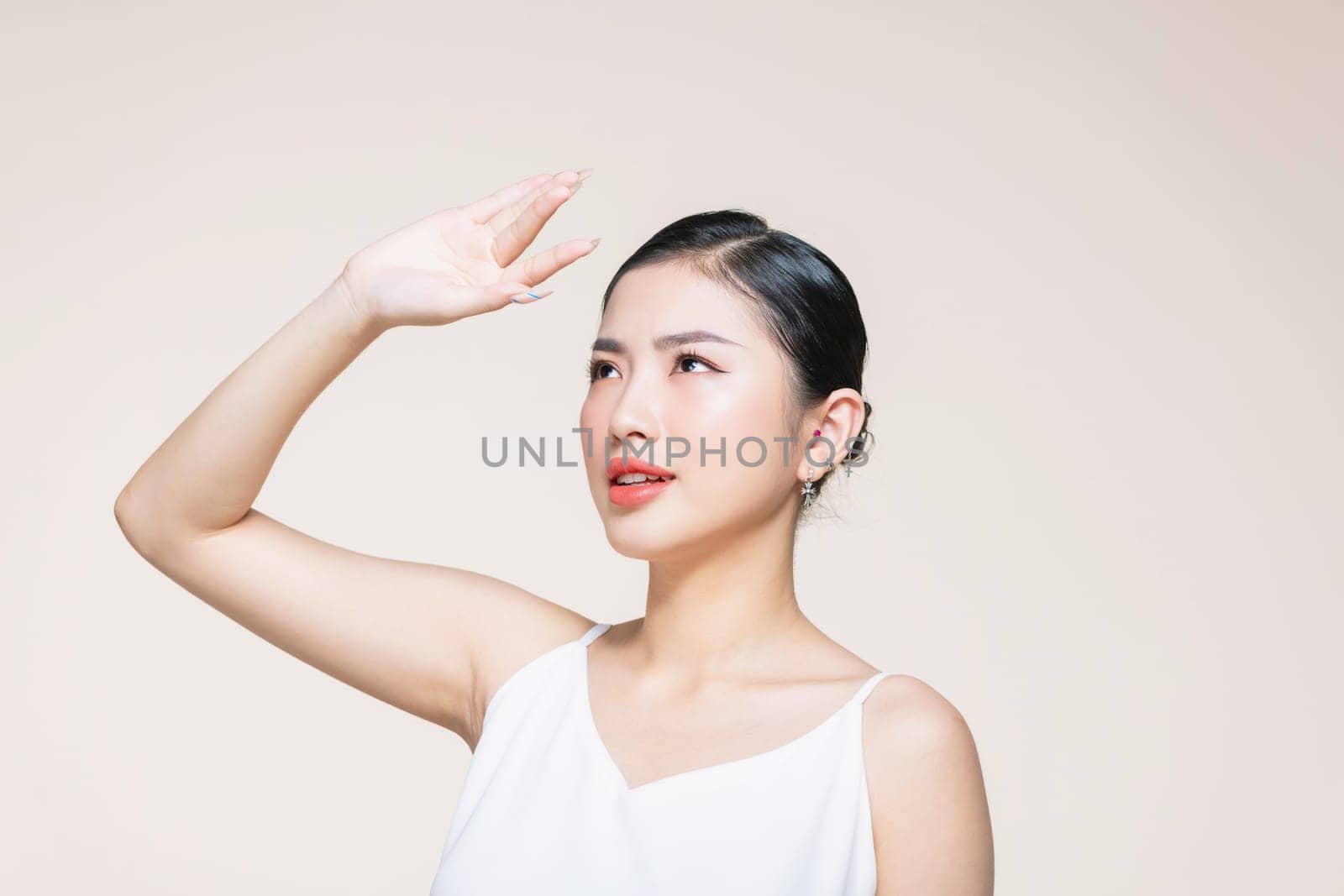 Woman covering her face from sun with her hand while standing against beige background