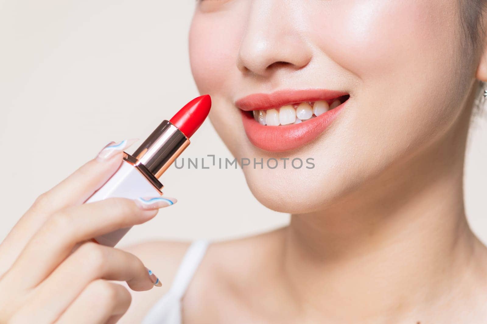 Young woman applying lipstick on beige