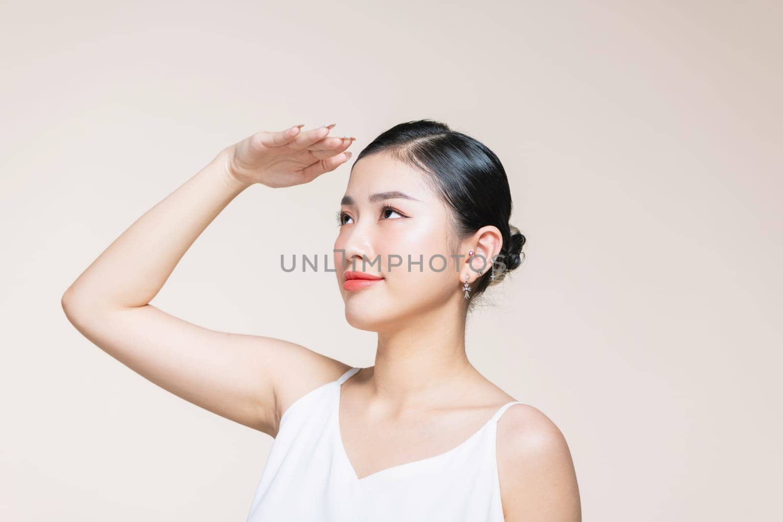 Woman covering her face from sun with her hand while standing against beige background