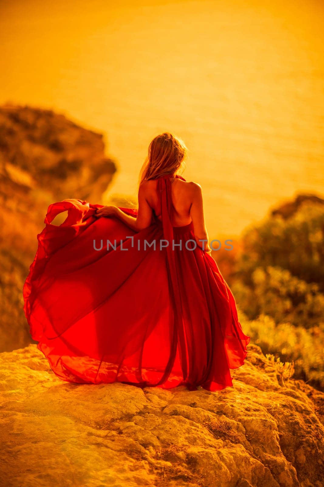 Woman sunset sea red dress, back view a happy beautiful sensual woman in a red long dress posing on a rock high above the sea on sunset