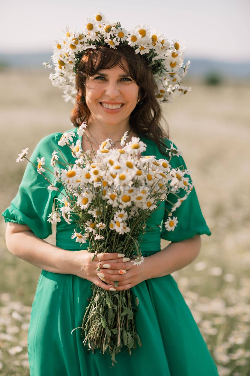 Happy woman in a field of daisies with a wreath of wildflowers on her head. woman in a green dress in a field of white flowers. Charming woman with a bouquet of daisies, tender summer photo by Matiunina