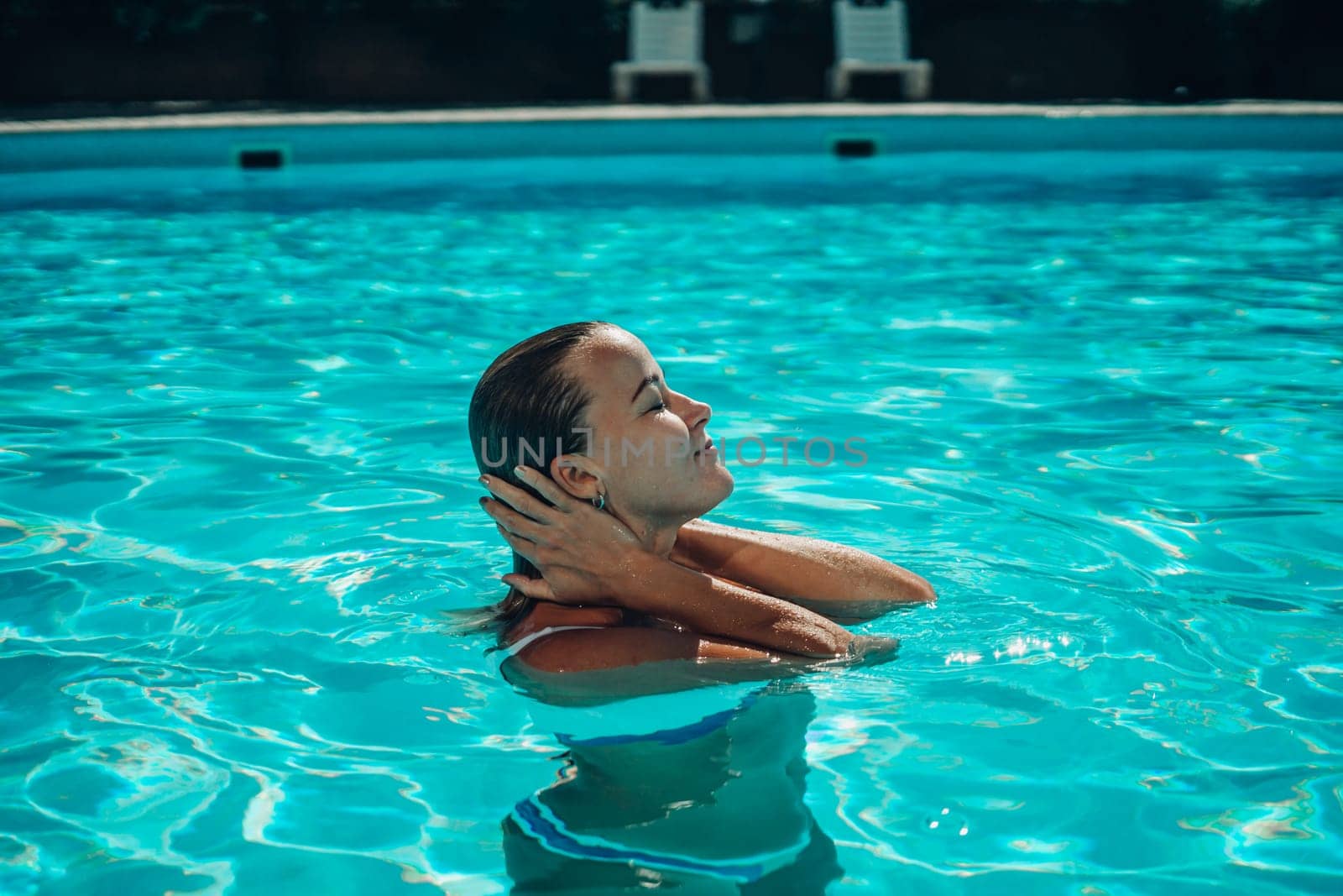 A woman is swimming in a pool. She is smiling and enjoying the water