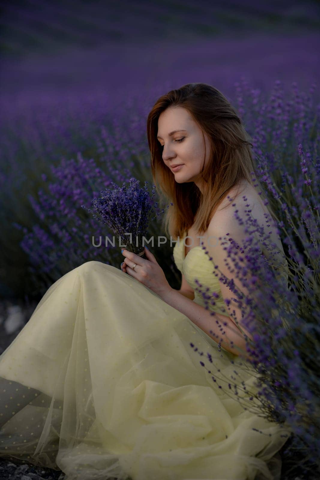 Woman poses in lavender field at sunset. Happy woman in yellow dress holds lavender bouquet. Aromatherapy concept, lavender oil, photo session in lavender.