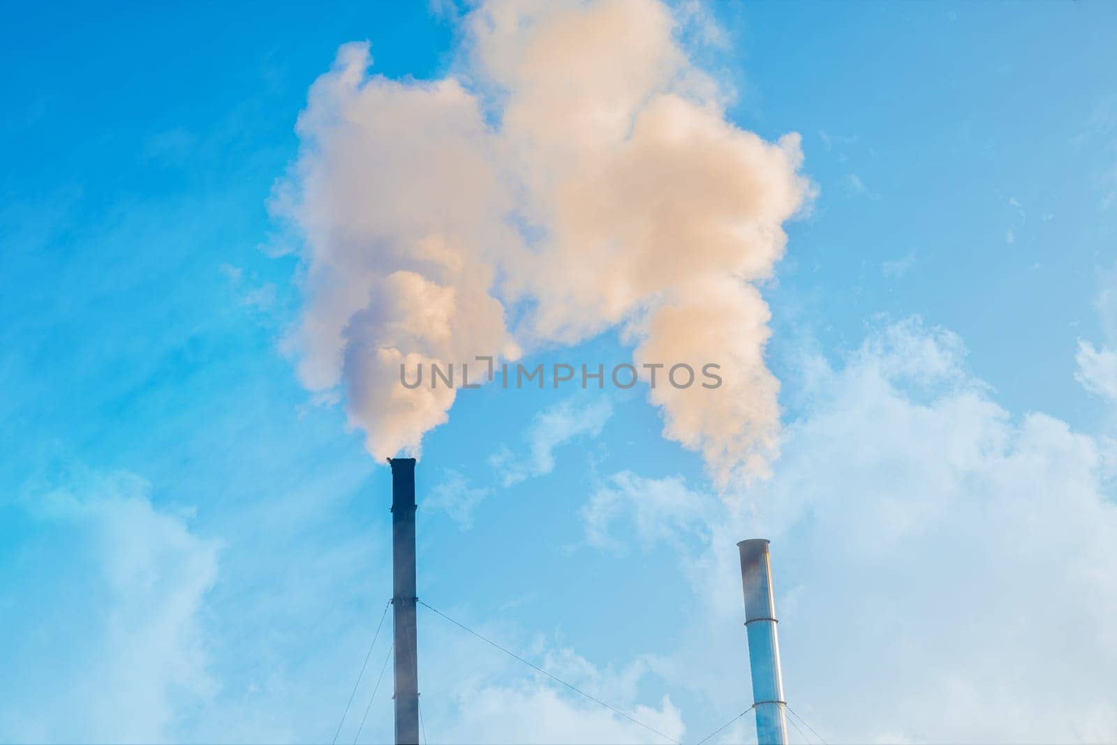 Two smoking factory chimneys against a blue sky. Increase CO2 and greenhouse gas emissions.