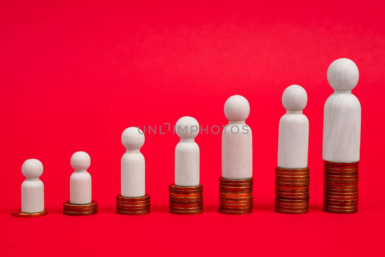 The concept of career growth and wealth increase. Wooden figurines stand on a ladder made of coins on a red background.