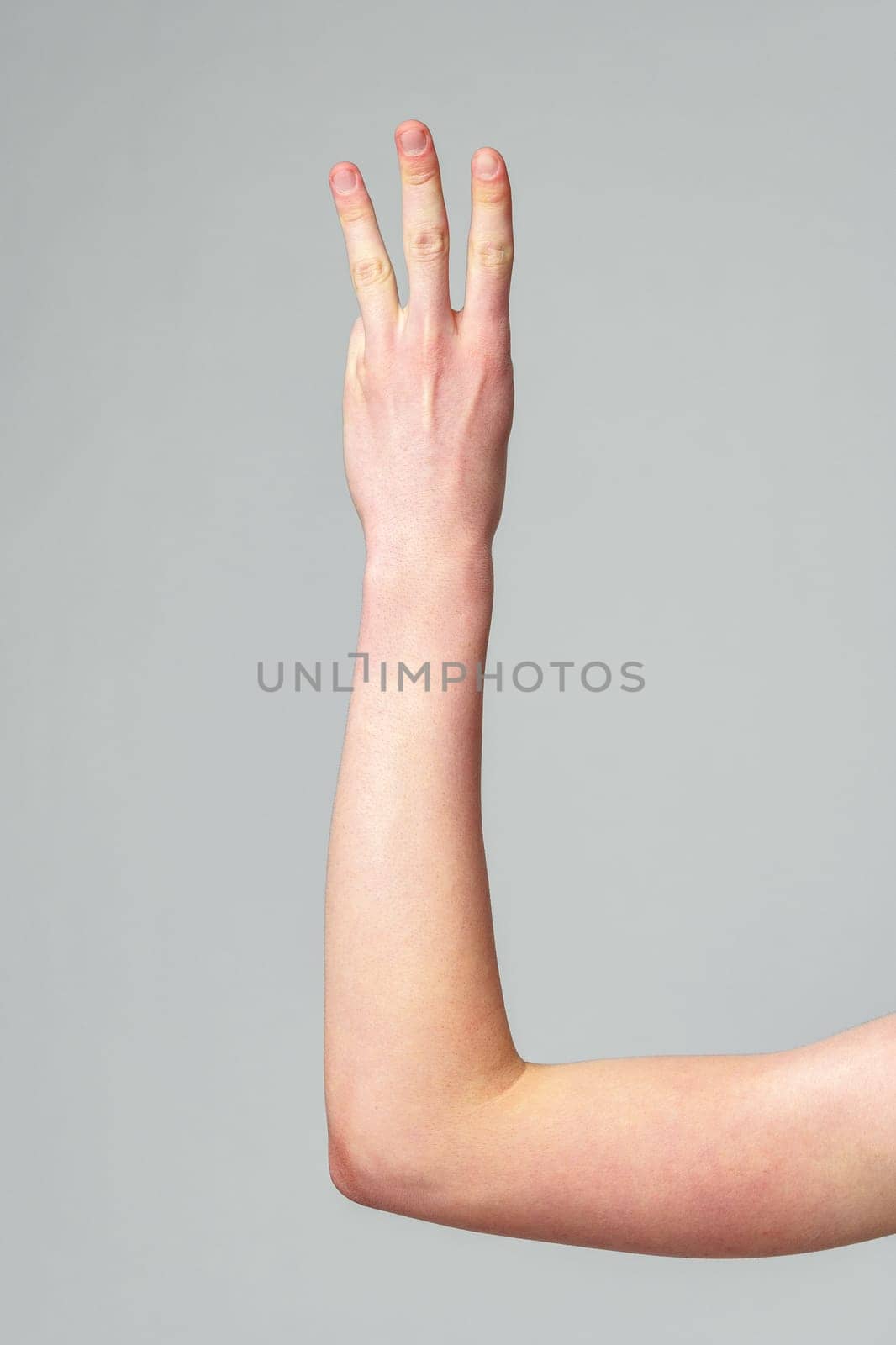 A human hand with fingers slightly apart is raised against a plain, neutral-colored background, signaling a nonverbal communication or waiting to be called upon.