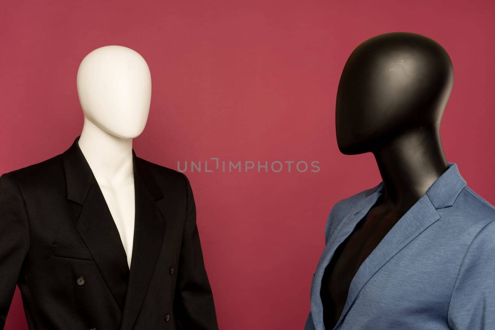 Two male mannequin in a black business suit and in a blue suit and white pants on a ruby background - image